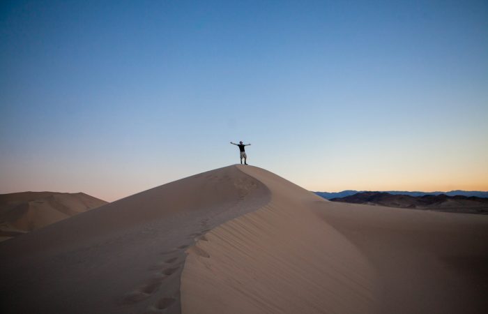 person raising both hands while standing on desert under blue and white sky